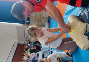 Uczennica kierowana przez ratownika wykonująca uciśnięcia klatki piersiowej na fantomie