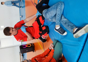 Ratownik w obecności dwóch uczniów wyjaśnia pozycję ustaloną boczną